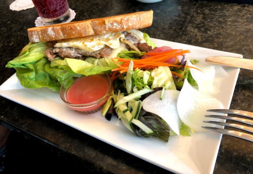 A sandwich with lettuce, meat, and an egg, served with a side salad and dressing on a white plate.