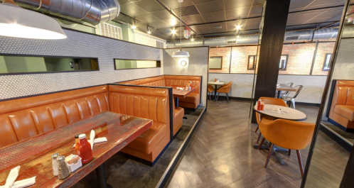 Interior of a modern restaurant featuring orange booths, wooden tables, and stylish decor with mirrors and soft lighting.