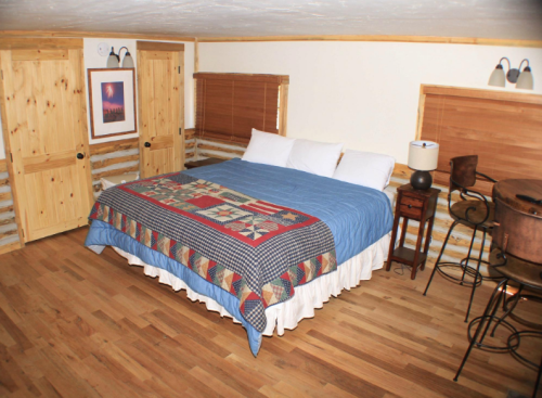 Cozy bedroom with a wooden floor, a large bed covered in a quilt, and rustic decor including a small table and chairs.