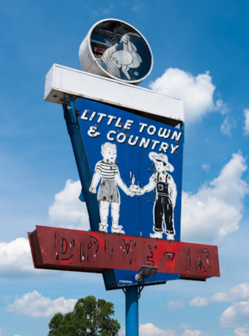 A vintage drive-in sign featuring two children holding hands, with "Little Town & Country" written above. Bright blue sky.