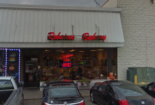 Exterior of Robaire's Bakery with a neon "Coffee Shop Open" sign and parked cars in front.