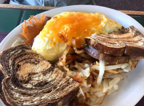 A plate of breakfast featuring an omelet topped with cheese, hash browns, and two slices of toasted bread.