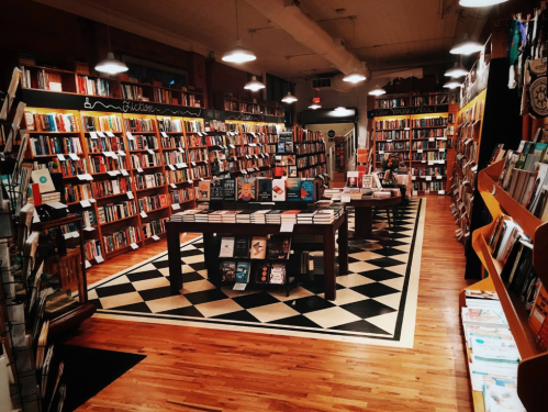 A cozy bookstore with wooden floors, shelves filled with books, and a central table displaying various titles.