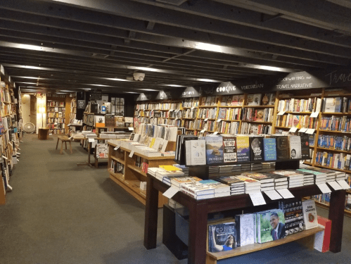 A cozy bookstore interior with shelves filled with books and wooden tables displaying various titles.