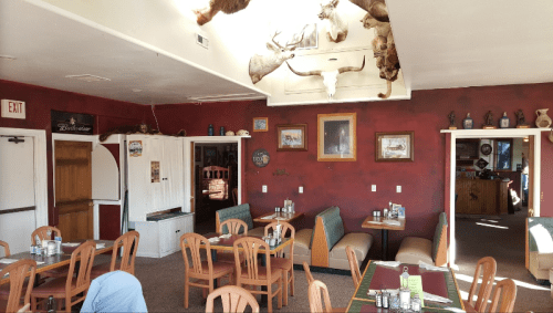 Cozy restaurant interior with wooden tables, green booths, and mounted animal heads on the ceiling. Warm, rustic decor.