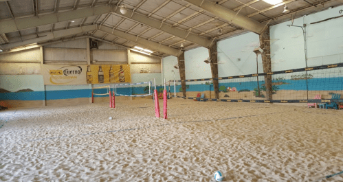 Indoor sand volleyball court with pink nets, surrounded by beach-themed murals and a sandy floor.