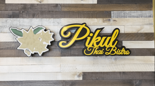 Sign for "Pikul Thai Bistro" with a floral design on a wooden wall background.
