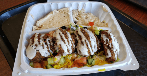 A takeout container with falafel, salad, hummus, and drizzled sauce.