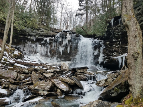 A frozen waterfall surrounded by icy rocks and trees, with icicles hanging from the cliff above.