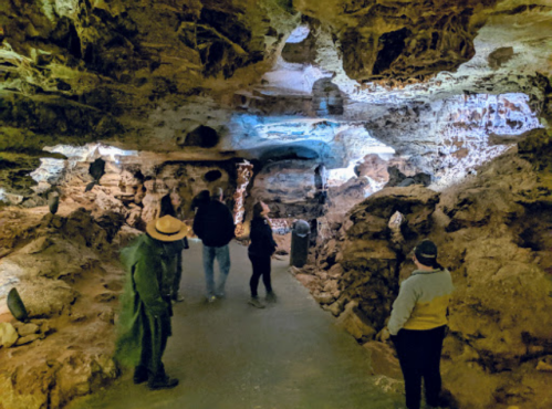 A group of people exploring a cave with rocky walls and illuminated areas, creating a mysterious atmosphere.