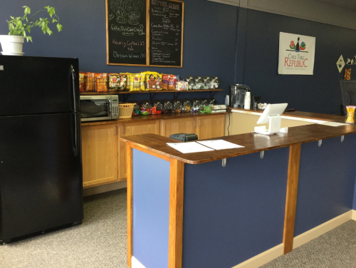 A cozy café counter with snacks, a fridge, and a chalkboard menu in a blue-walled space.
