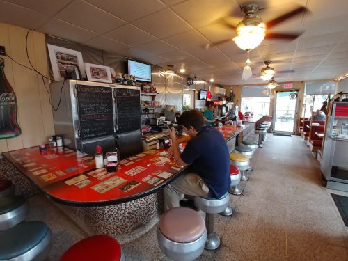 A diner interior with a red counter, a lone customer sitting, and vintage decor, creating a nostalgic atmosphere.