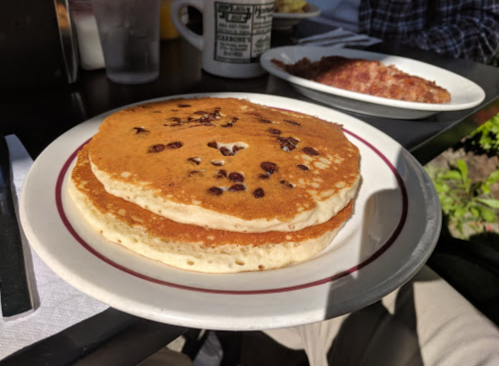 A plate with two fluffy pancakes topped with chocolate chips, served at a restaurant table.