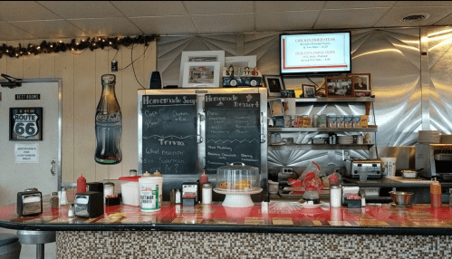 A diner counter with a chalkboard menu, condiments, and a dessert display, decorated for the holidays.