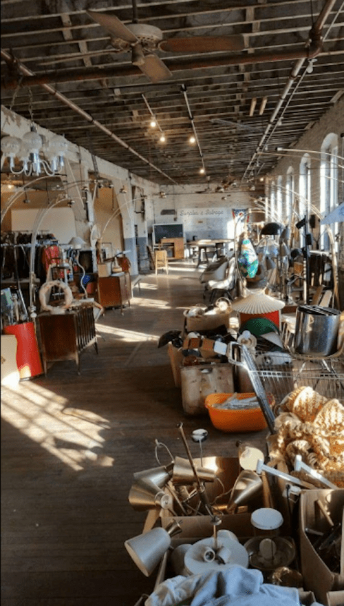 A spacious vintage shop filled with various furniture, lamps, and decor items, illuminated by natural light.