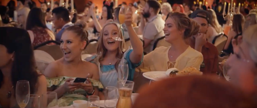 A lively group of friends at a celebration, smiling and raising glasses in a festive atmosphere.