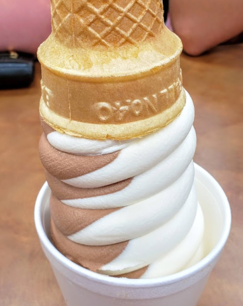 A soft-serve ice cream cone with chocolate and vanilla swirls, placed in a white cup on a table.