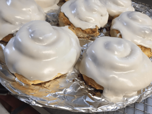 Freshly baked cinnamon rolls topped with creamy white icing, arranged on a foil-lined tray.