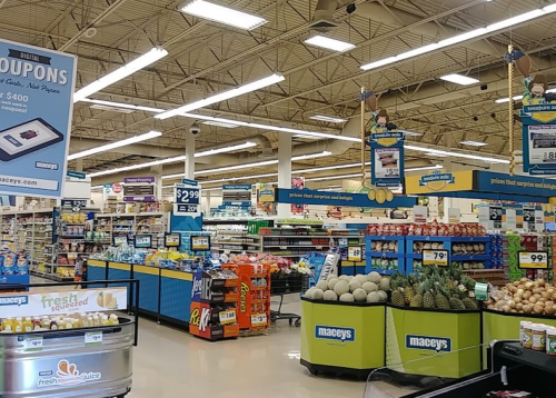 A grocery store aisle filled with various products, including fruits, vegetables, and promotional signs.