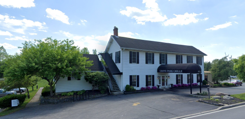 A white two-story building with a black awning labeled "Grove Park Grille," surrounded by greenery and flowers.