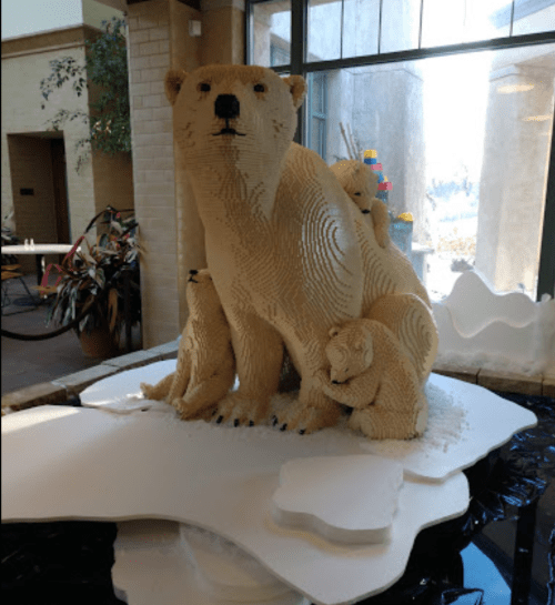 A large polar bear sculpture made of cream-colored blocks, surrounded by smaller bear cubs, on a snowy base.