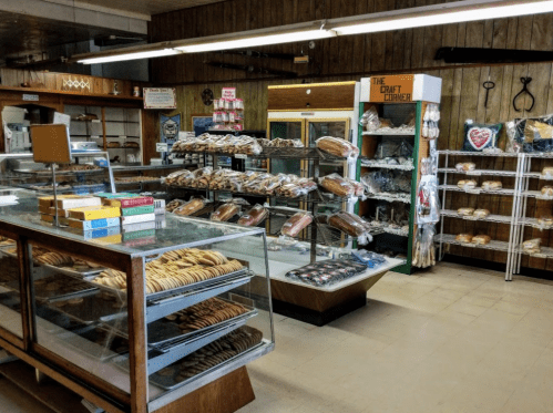 A cozy bakery interior with glass display cases filled with various baked goods and a shelf of packaged treats.