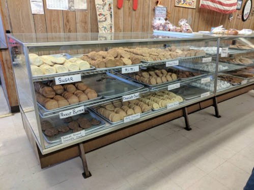 A display case filled with various types of cookies, labeled by flavor, in a cozy bakery setting.