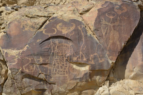 Petroglyphs carved into a rocky surface, depicting abstract figures and symbols against a natural stone backdrop.