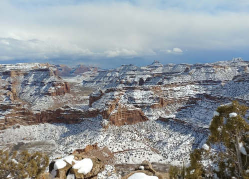 Snow-covered canyons and cliffs under a cloudy sky, showcasing a stunning winter landscape.