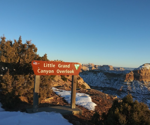 Sign for Little Grand Canyon Overlook with a scenic view of canyons and snow-covered ground under a clear blue sky.