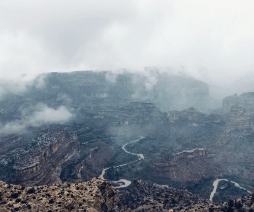 A misty canyon landscape with winding roads and rocky cliffs, shrouded in clouds.