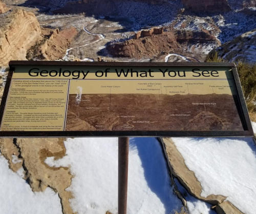 Sign titled "Geology of What You See" with geological features and descriptions, set against a snowy canyon landscape.