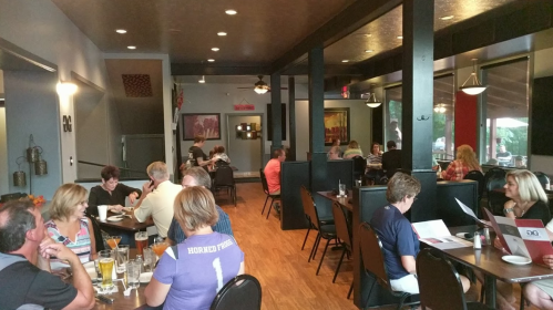 A busy restaurant interior with diners at tables, enjoying meals and drinks in a warm, inviting atmosphere.