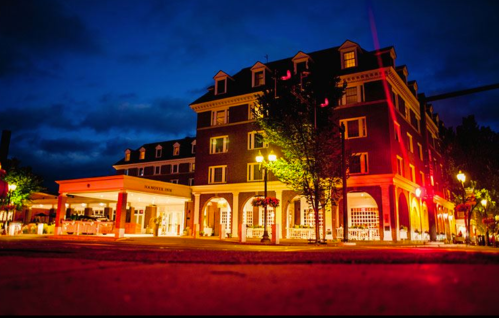 A brick hotel illuminated at night, featuring arched entrances and trees, with a cloudy sky in the background.