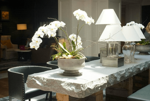 A modern table with a textured stone surface, featuring white orchids and stylish lamps in a bright, elegant setting.