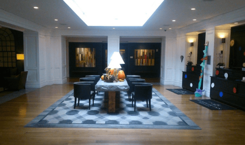 A spacious hotel lobby with a central table, decorative items, and modern art on the walls, featuring wooden flooring.