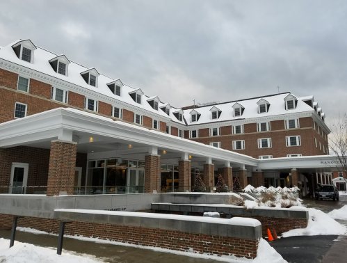 A brick hotel with a white snow-covered roof, surrounded by snow, under a cloudy sky.