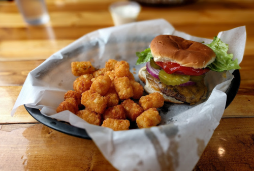 A plate with a burger topped with lettuce, tomato, and onion, alongside a serving of crispy tater tots.