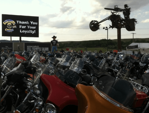A crowded motorcycle rally with numerous bikes and a large sign thanking attendees for their loyalty.