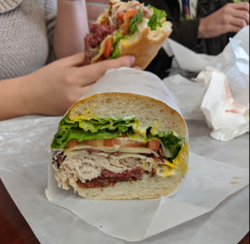 A close-up of a sandwich with layers of turkey, roast beef, lettuce, tomato, and mustard on a hoagie roll.