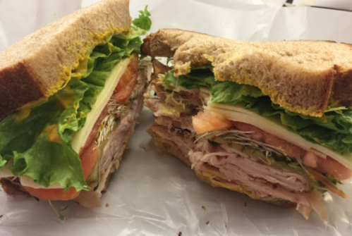 A close-up of a sandwich with layers of turkey, lettuce, tomato, and mustard on whole grain bread, cut in half.