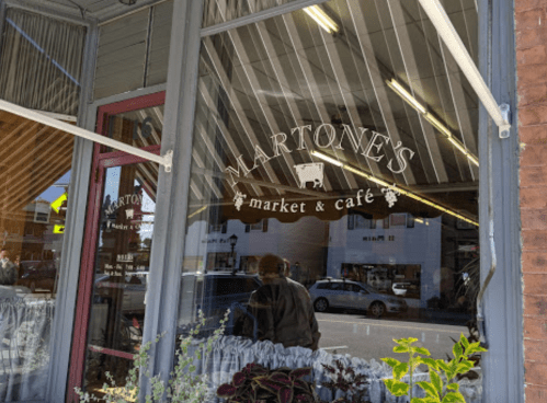 Window reflection of Martone's Market & Café, featuring a sign and plants in the foreground.