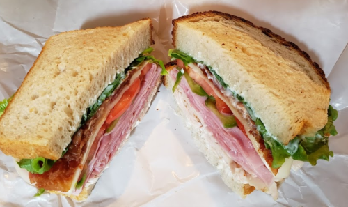 A freshly cut sandwich with layers of ham, lettuce, tomato, and mayonnaise between two slices of toasted bread.