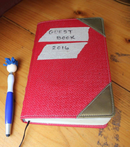 A red guest book labeled "2016" next to a blue and white pen on a wooden table.