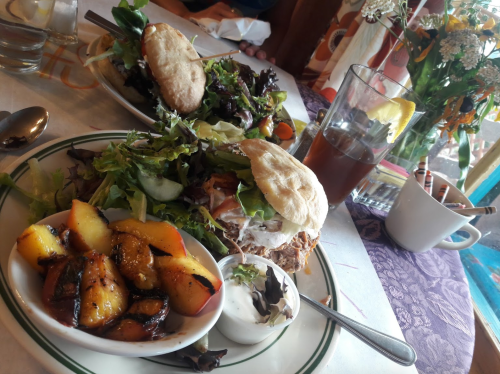 A plate with a sandwich, mixed greens, and a side of roasted potatoes, with a glass of iced tea in the background.