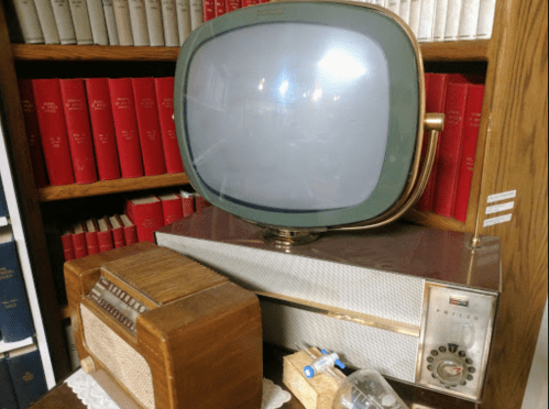 A vintage television and radio set displayed on a shelf with red books in the background.