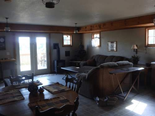 Cozy living room with a sofa, dining table, and large windows, featuring warm lighting and rustic decor.