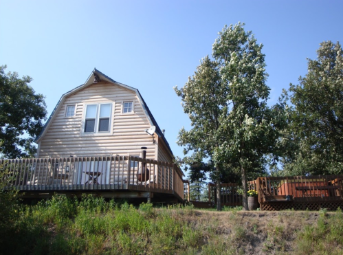 A wooden cabin with a deck surrounded by trees under a clear blue sky.