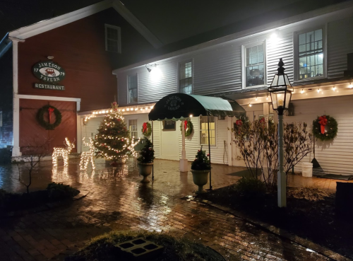 A festive restaurant exterior adorned with wreaths, lights, and a Christmas tree, reflecting on a rainy night.