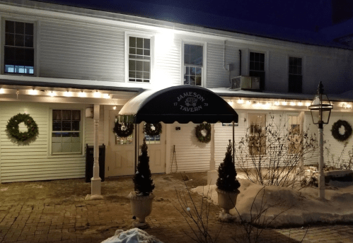 Exterior of Jameson Tavern at night, featuring festive wreaths, snow, and a green awning with the tavern's name.